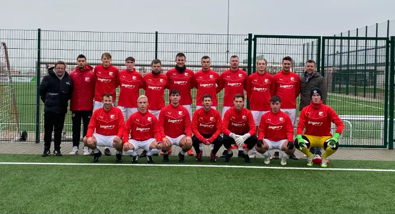 Fussballmannschaft in roten Trikots, zwei Reihen auf einem Kunstrasenplatz