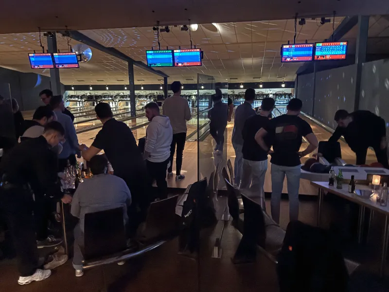 Grössere Gruppe beim Bowling vor beleuchteten Bahnen und Anzeigemonitoren